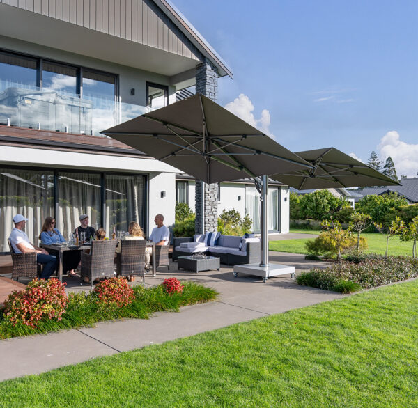 A family sits at a table under a dual-canopy outdoor umbrella that tilts